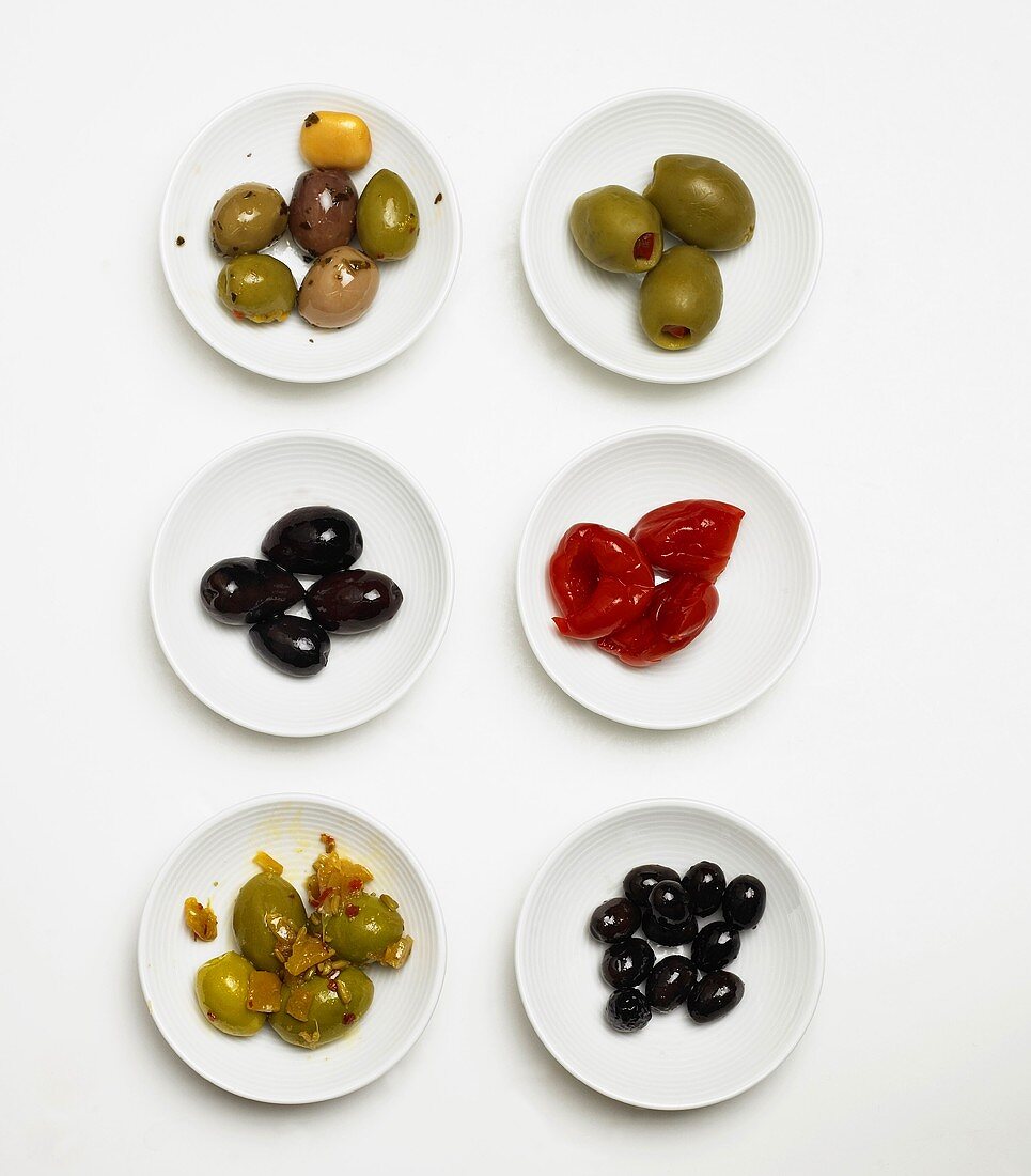 Verschiedene eingelegte Oliven & Peperoni auf weissen Tellern