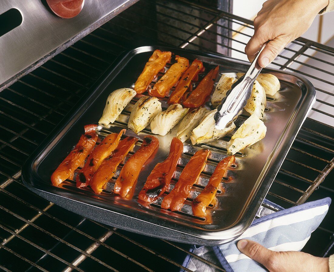 Flipping Vegetables with Tongs on a Broiler Pan in the Oven