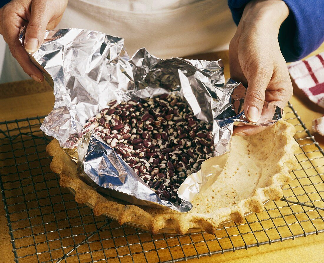 Folie mit getrockneten Bohnen vom Kuchenboden entfernen
