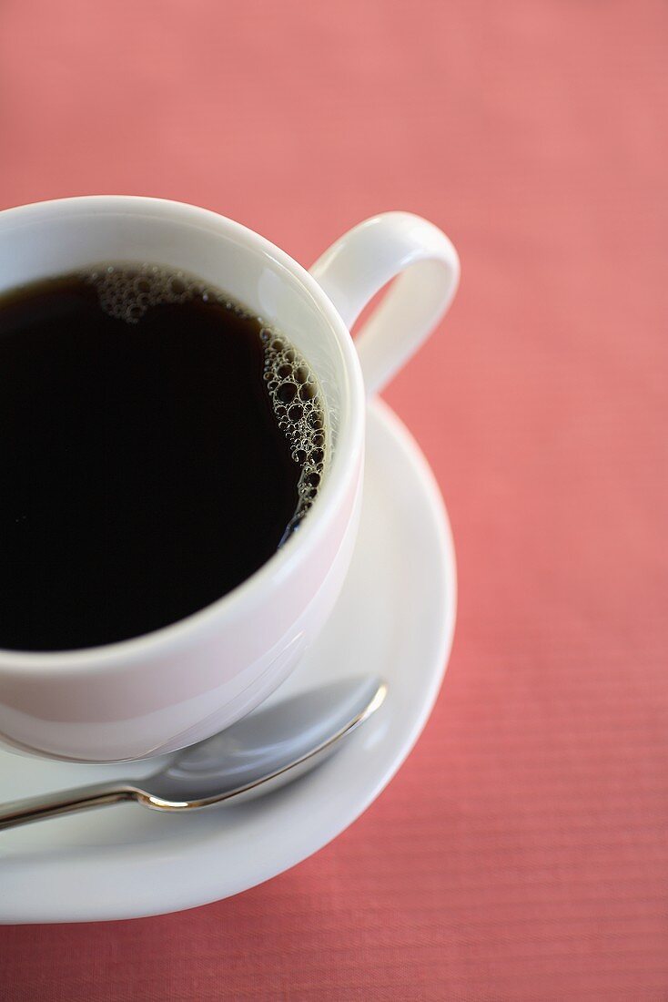 Eine weiße Tasse mit schwarzem Kaffee auf rosa Untergrund