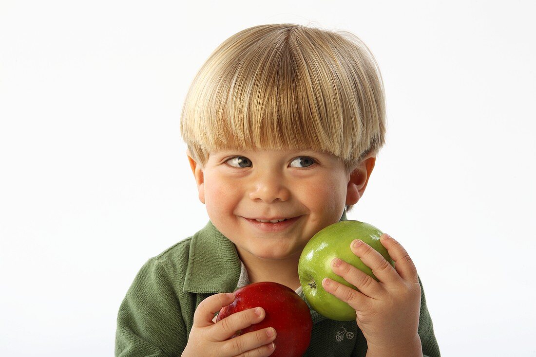 Ein lächelnder kleiner Junge hält zwei Äpfel in den Händen