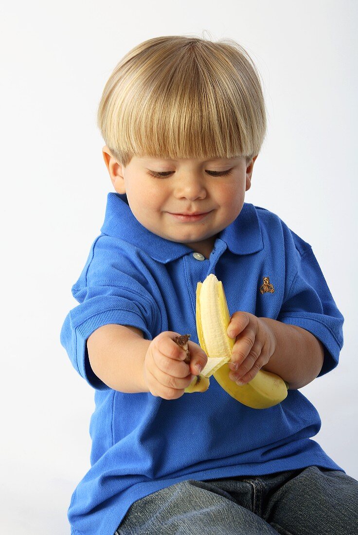 Ein sitzender kleiner Junge schält eine Banane