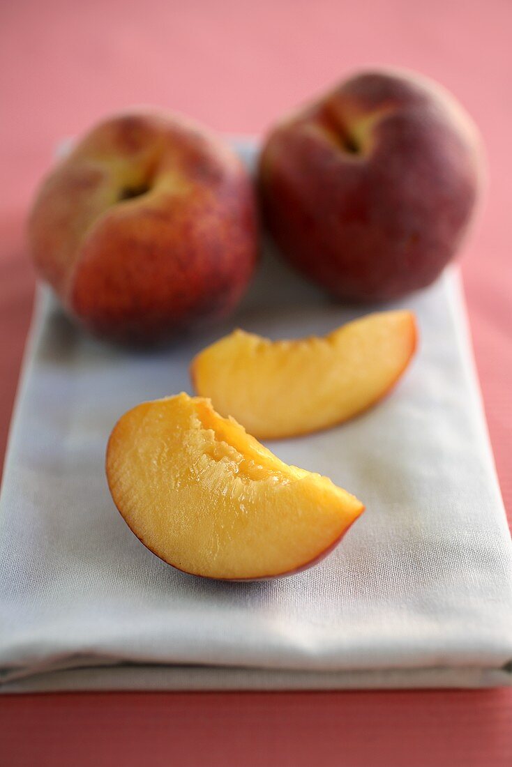 Two Peach Slices and Two Whole Peaches on a Folded Dish Cloth