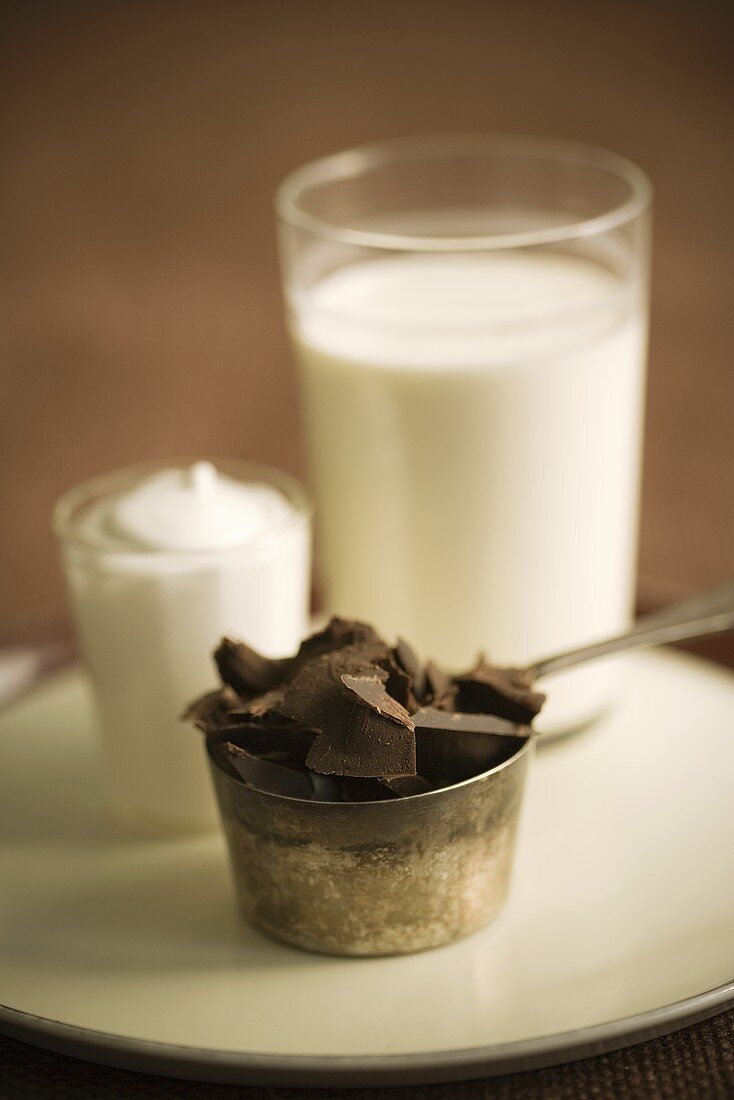 Schokoladenstücke in Metallschälchen, ein Glas Milch, Sahne