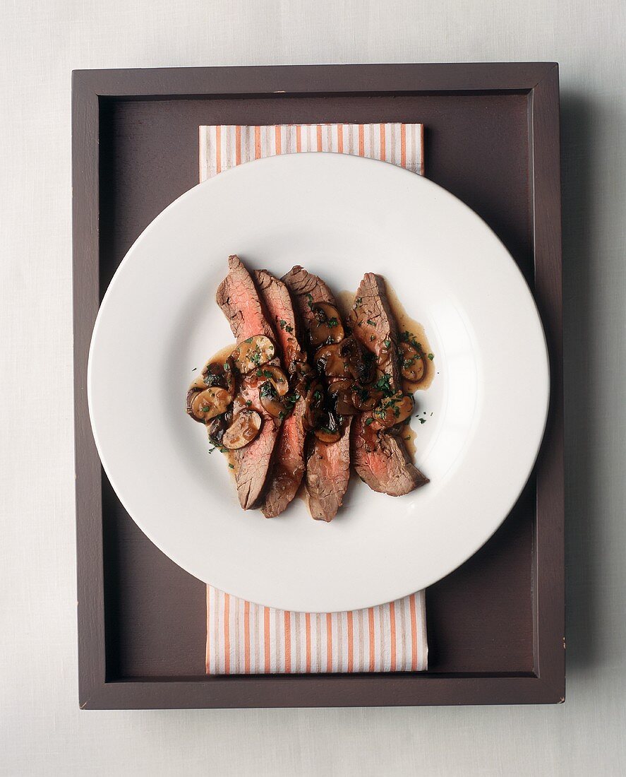 Steakscheiben mit Pilzsauce auf weißem Teller (Draufsicht)