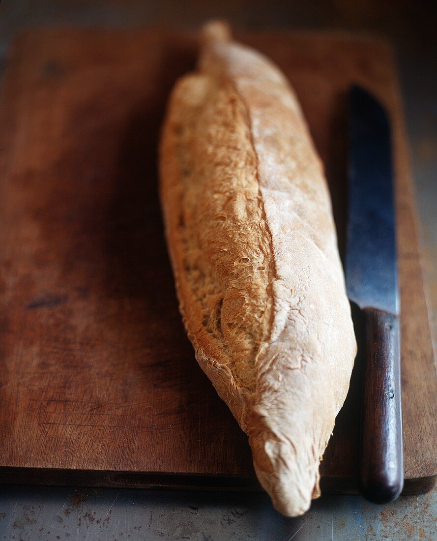 Baguette mit altem Messer auf Schneidebrett