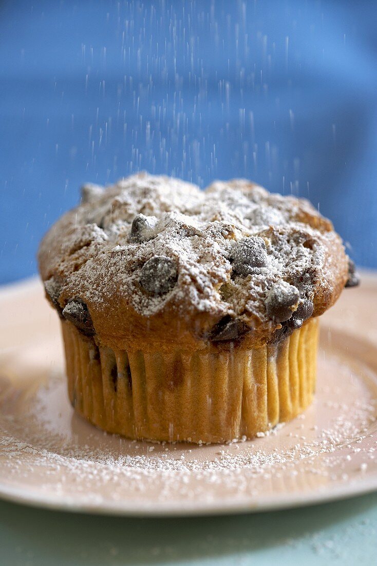 Sprinkling a Chocolate Chip Muffin with Powdered Sugar