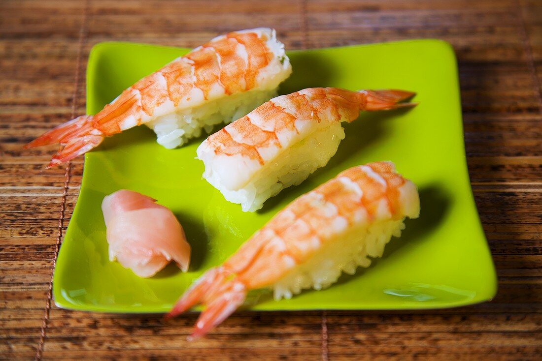 Three prawn nigiri sushi on green plate