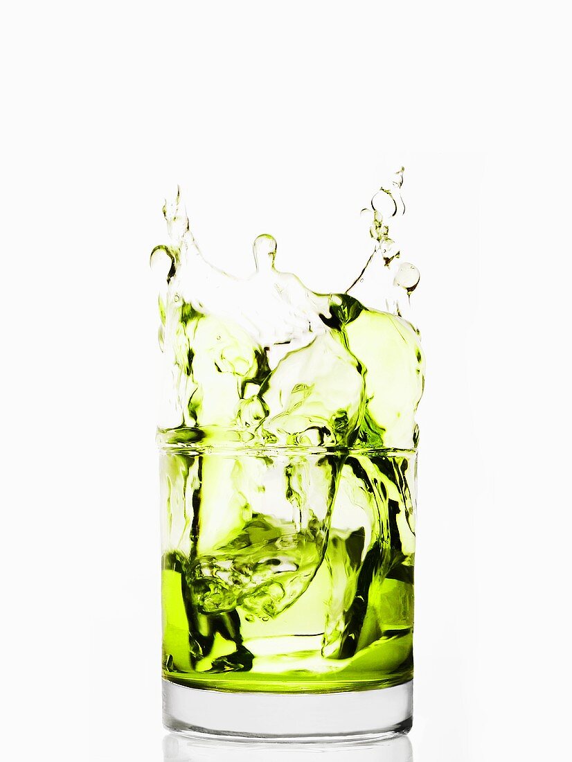 Eiswürfel fällt in Glas mit grüner Flüssigkeit