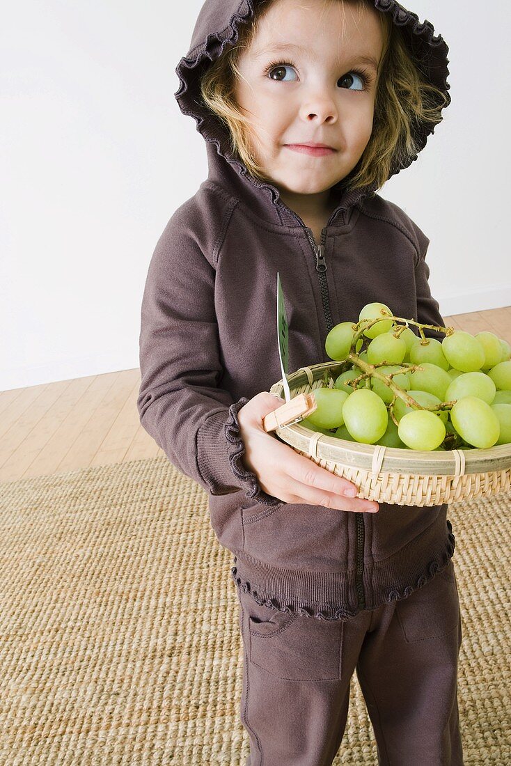 Kleines Mädchen hält Korb mit grünen Trauben