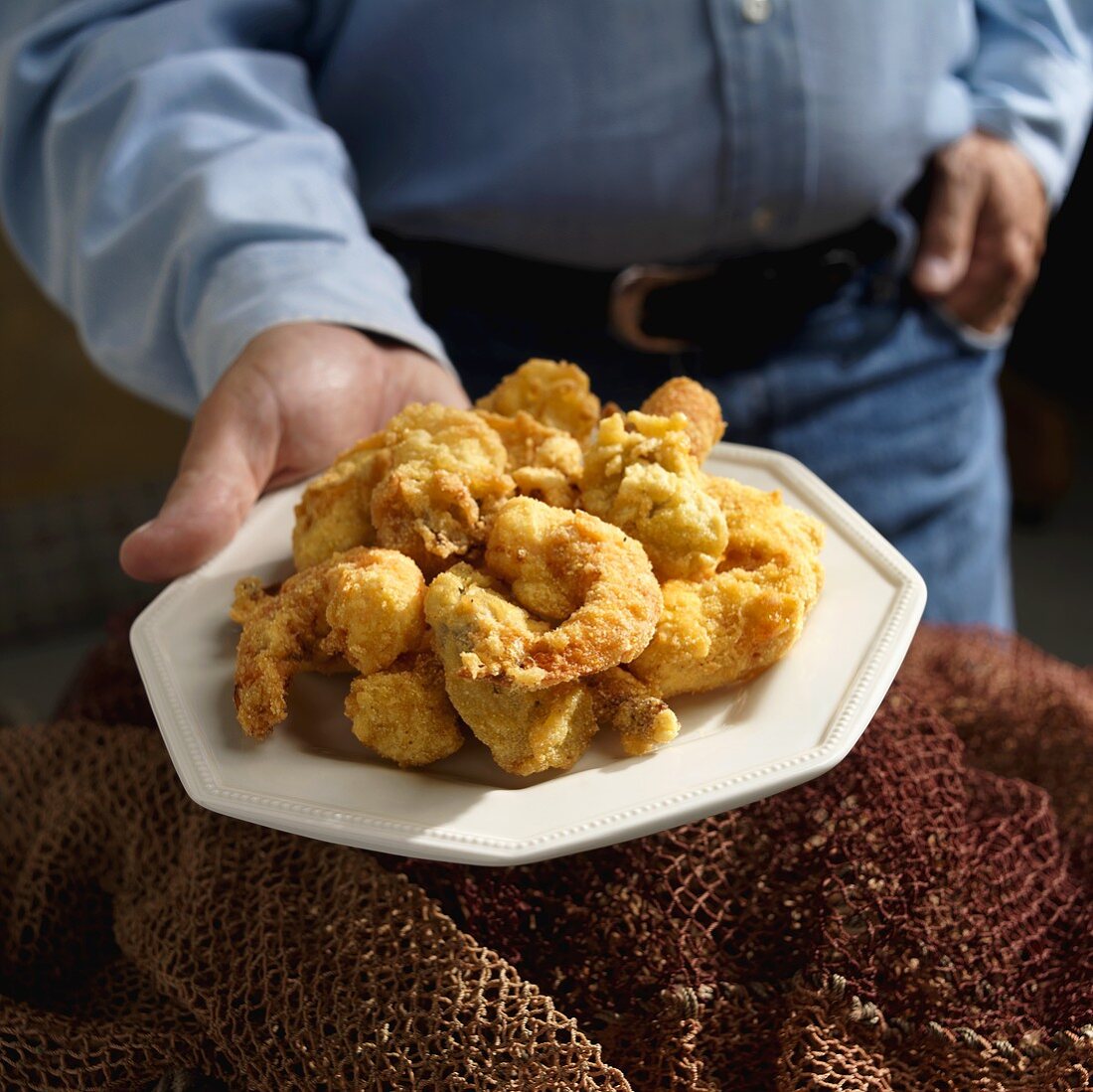 Mann hält Teller mit frittierten Shrimps und Austern