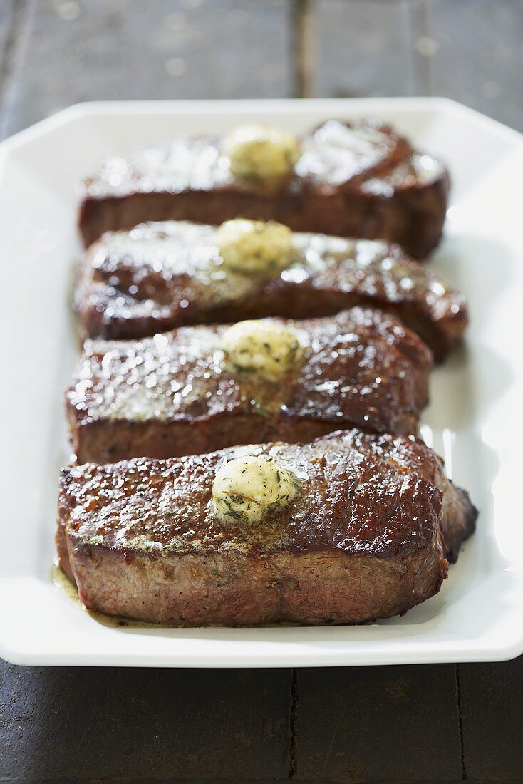 Four NY Strip Steaks with Herb Butter on a Platter