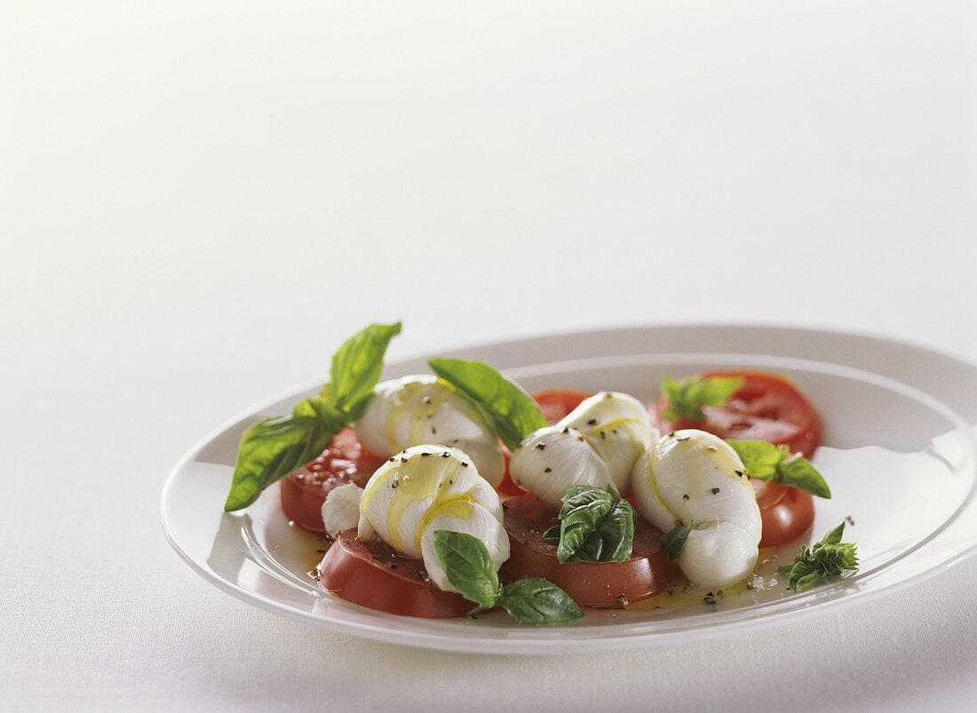 Caprese Salad with Roma Tomatoes and Knots of Mozzarella on White Plate