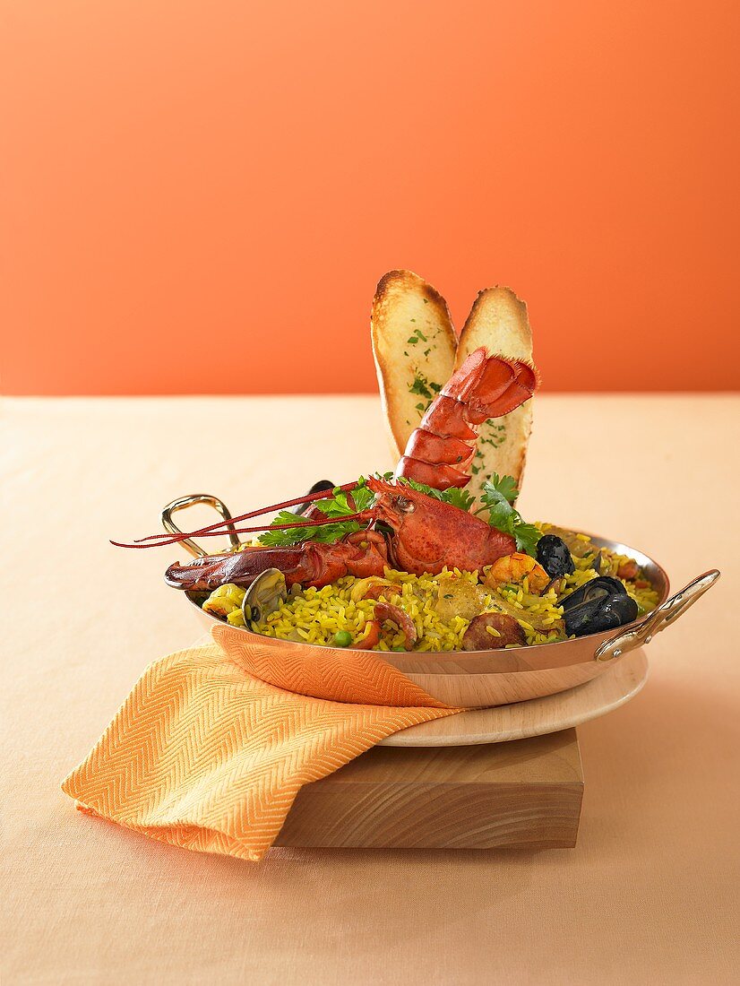 Paella mit Hummer und Knoblauchbrot in einem Pfännchen