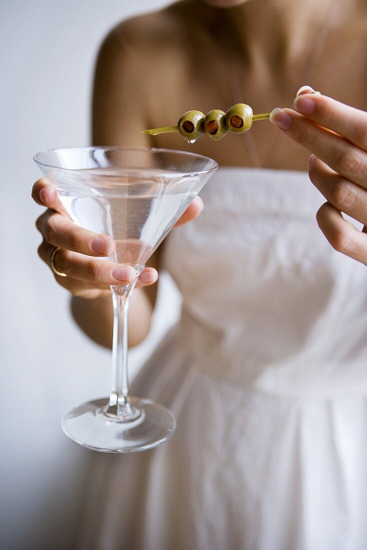 Frau hält Martini mit aufgespießten Oliven
