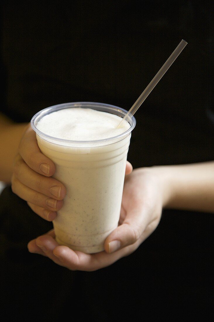 Hände halten einen Becher Kardamom-Lassi mit Strohhalm