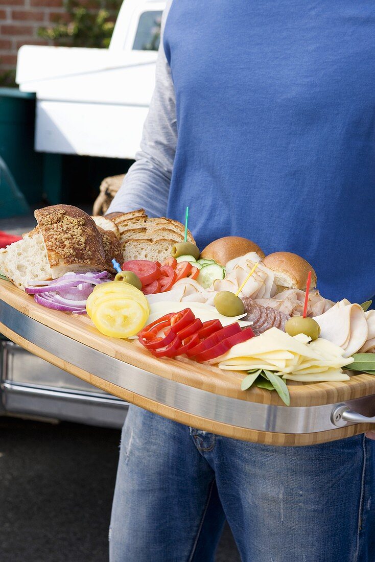 Person hält Brett mit Zutaten für Sandwiches