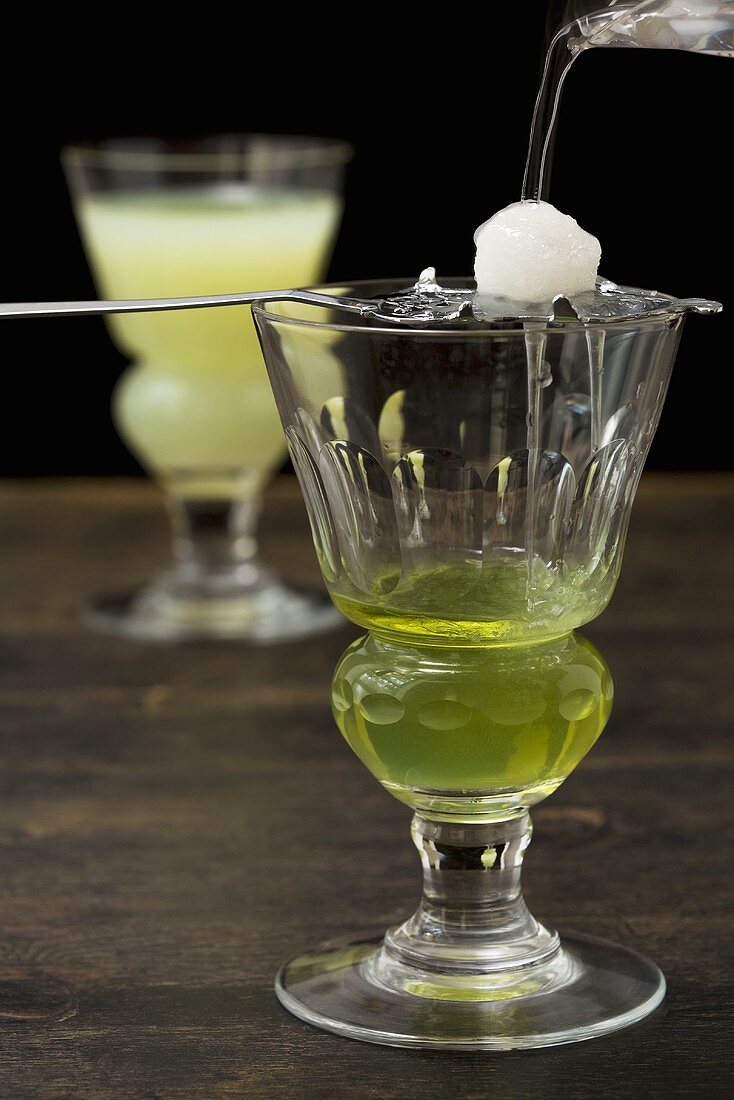 Zuckerwürfel auf Absinthlöffel mit Wasser auflösen