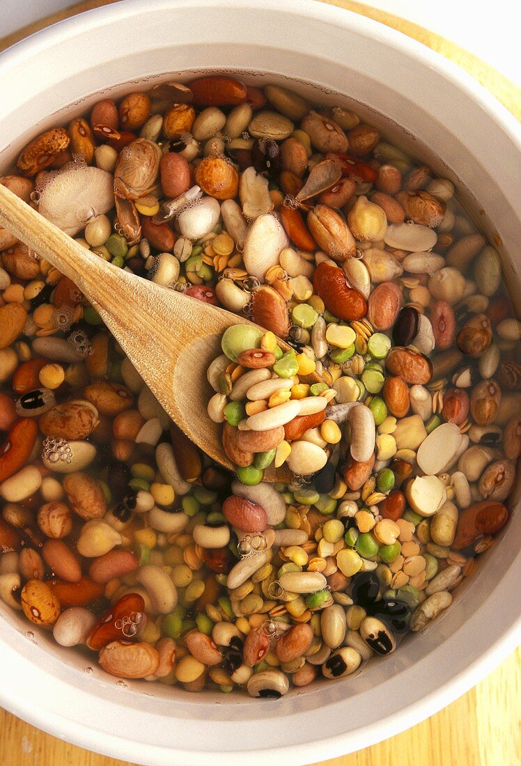 Mixed Beans and Lentils Soaking in a Bowl; Wooden Spoon