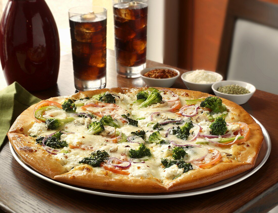Ganze Gemüsepizza mit Brokkoli, im Hintergrund Cola mit Eis