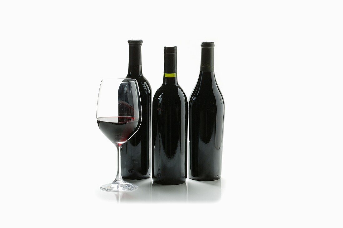 Glass of Red Wine with Three Wine Bottles