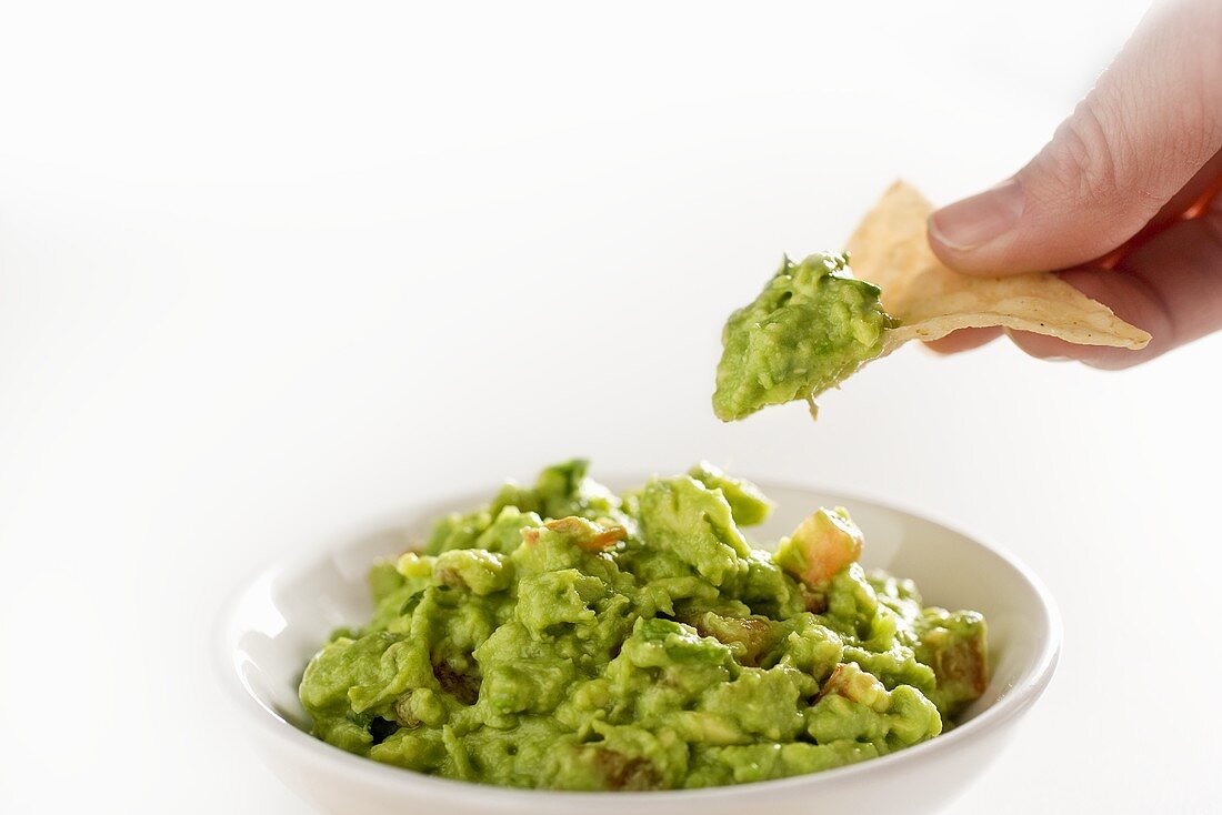 Hand hält Tortillachip mit Guacamole