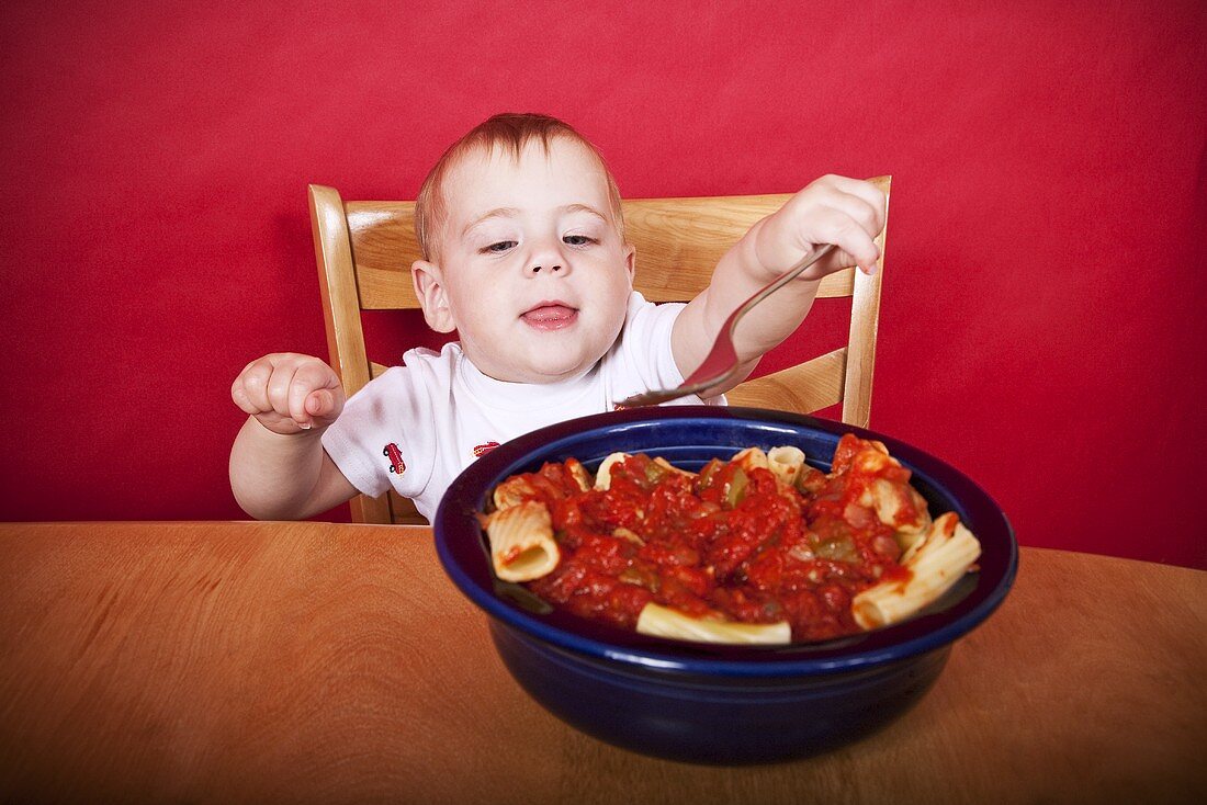 Baby mit Gabel vor Nudeln mit Tomatensauce