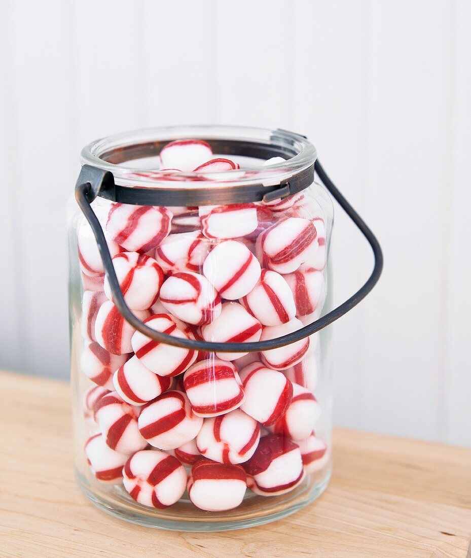 Viele rot-weiss gestreifte Pfefferminzbonbons im Henkelglas