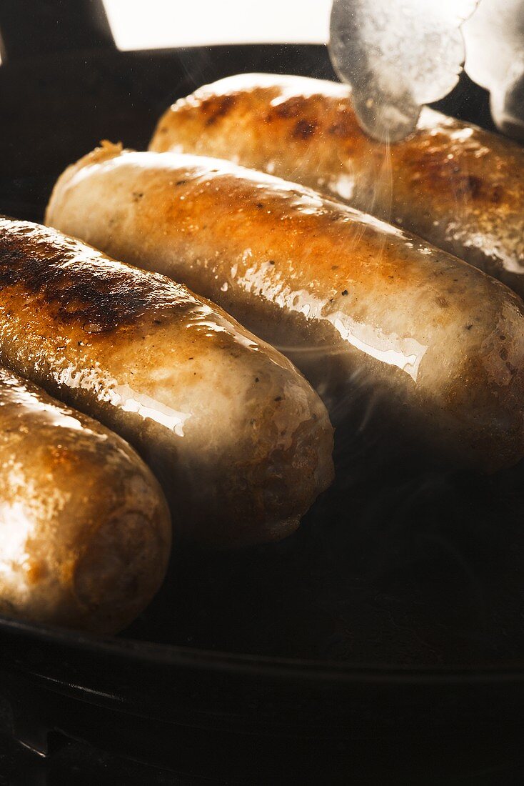 Sausages Cooking in Skillet; Tongs