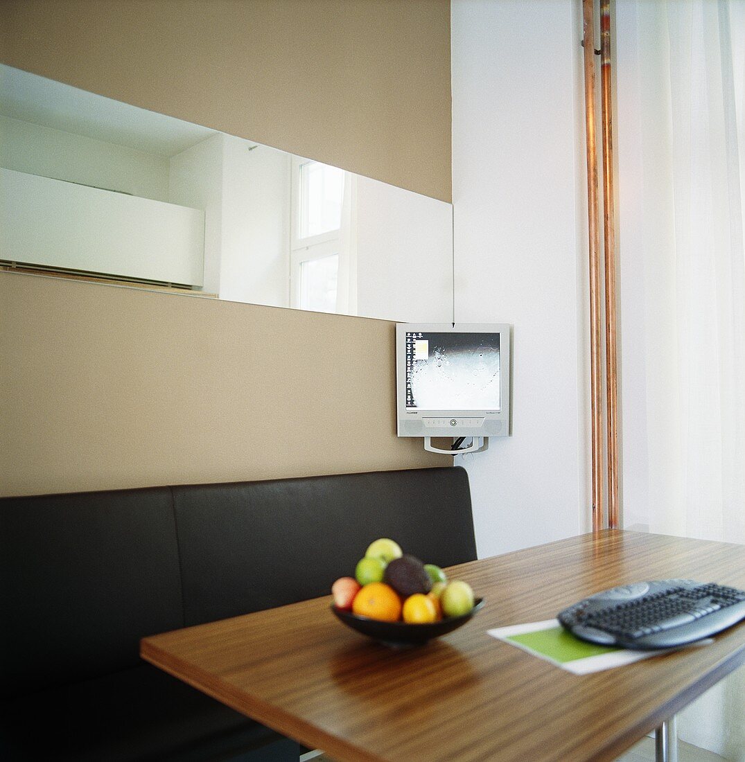 A fruit bowls and a keyboard on a table with a monitor in the background