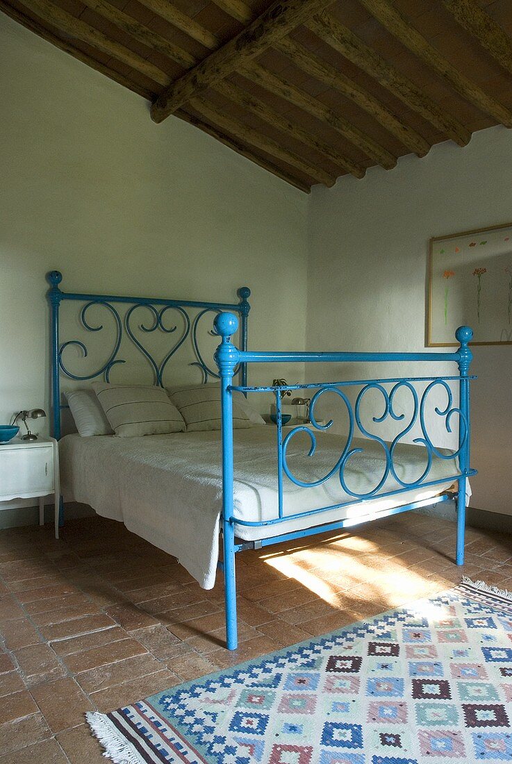 A blue wrought iron bed in a bedroom with a terracotta floor
