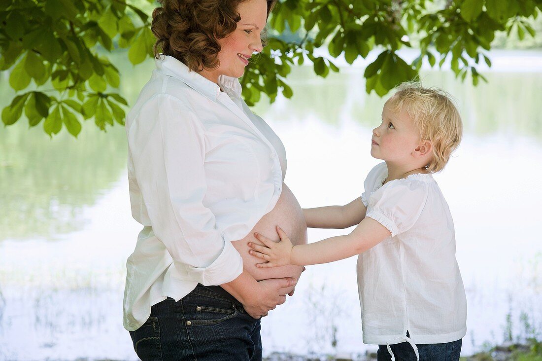 A little girl holding her pregnant mother's belly