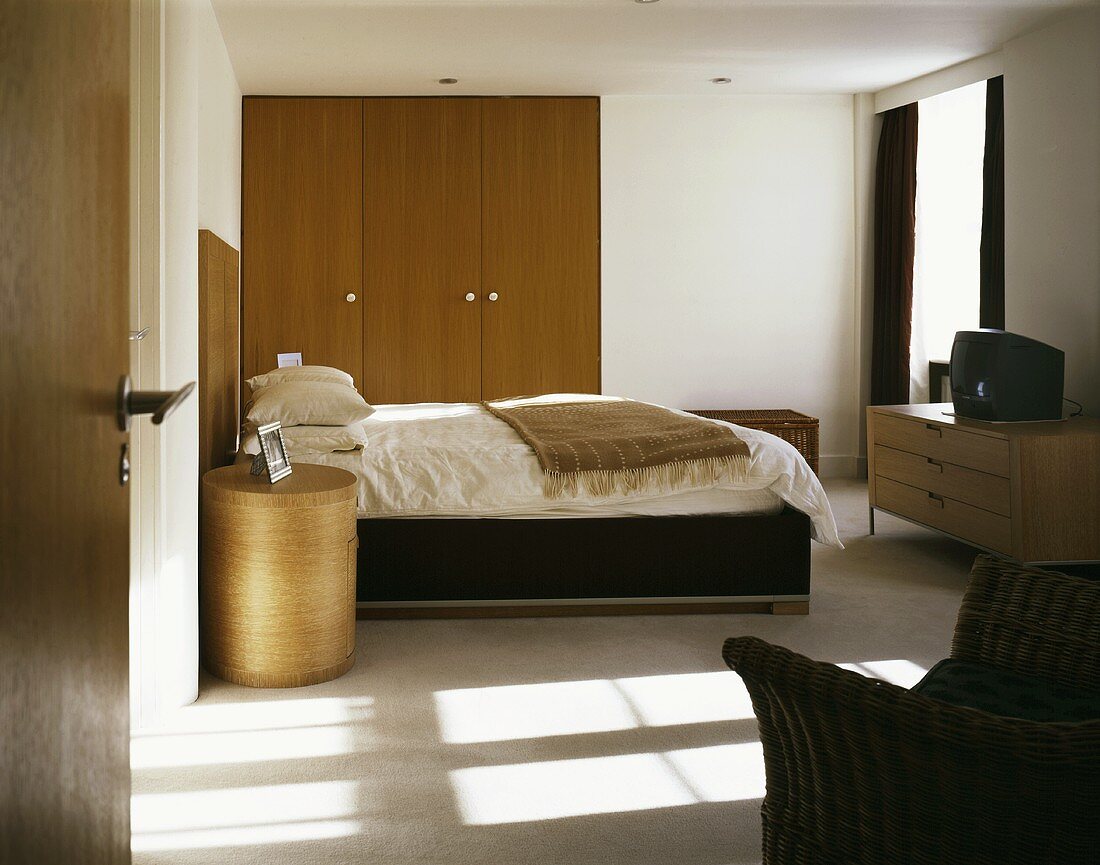 View through an open door into a modern bedroom with a double bed and built-in wooden closet