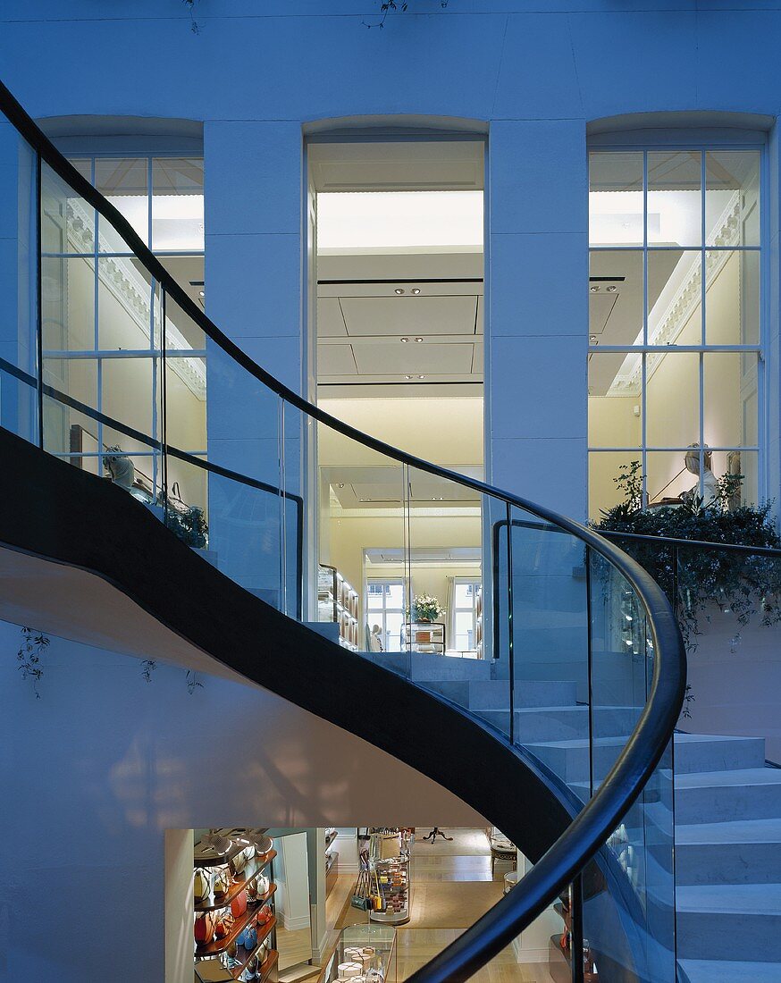 Geschwungene Aussentreppe in Dämmerlichtstimmung und Blick in beleuchtete loftartige Wohnung