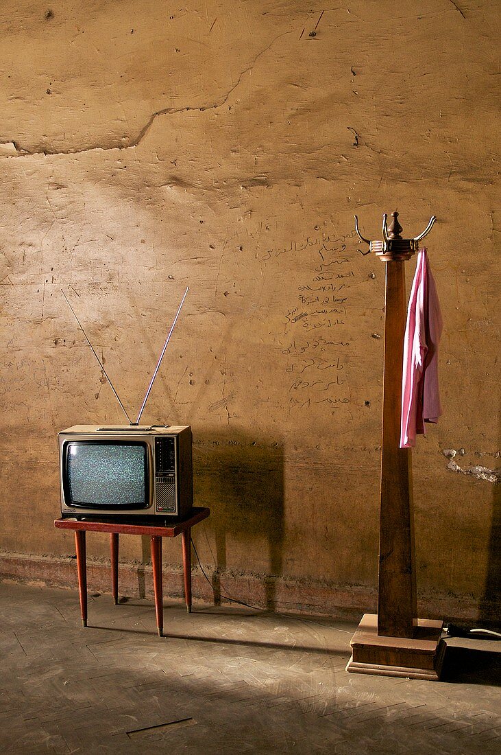 alter Fernseher auf Tischchen, neben Garderobenständer aus Holz