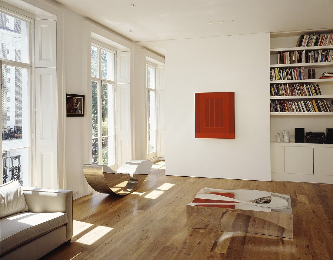 Open living area in a grand house with chrome coffee table on wood flooring in front of a partition with a library