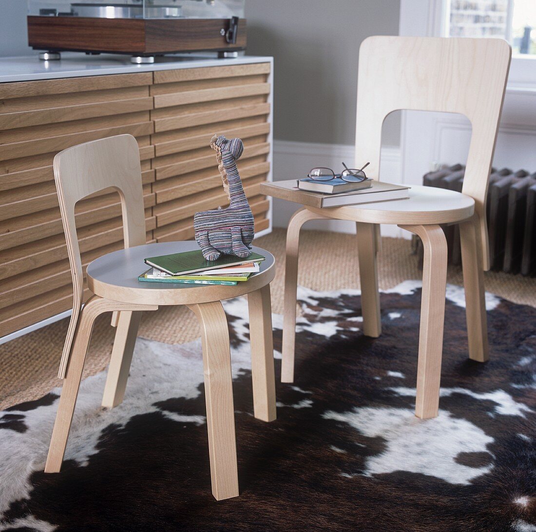 Two modern wooden chairs in front of a sideboard with a record player on it