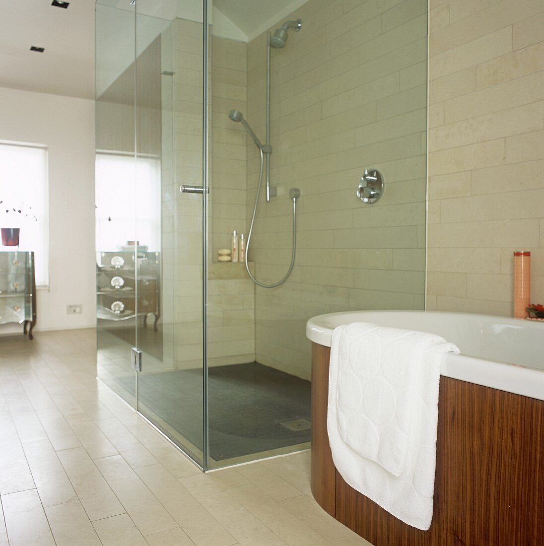 Walk in shower with glass wall next to a free standing bathtub