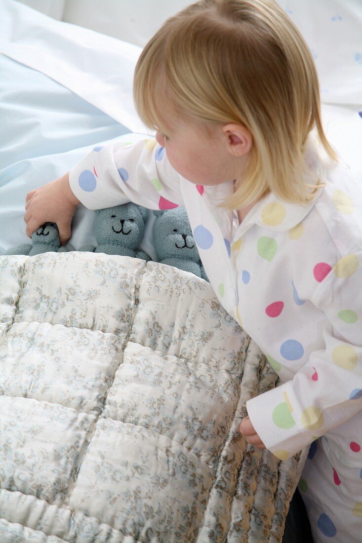 Little girl tucking her plush animals into bed