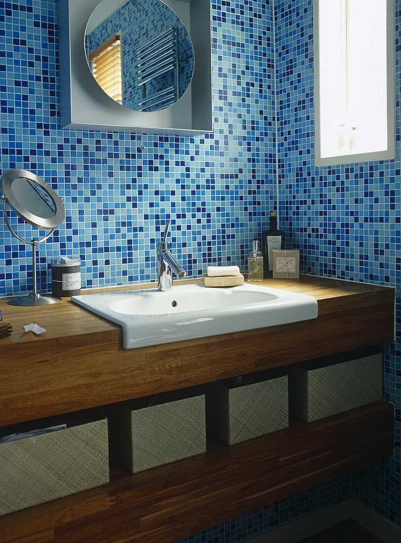 Waschtisch aus Holz und moderner Spiegel vor blauen Mosaikfliesen in Badezimmerecke