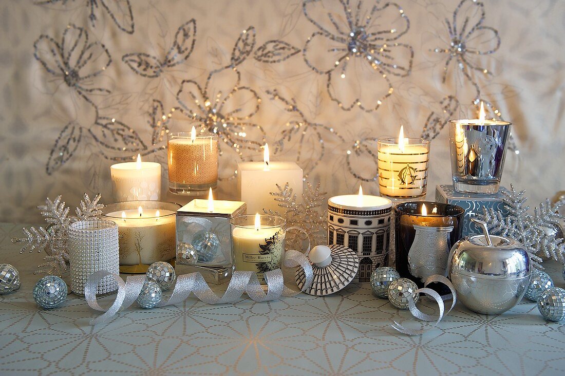 Burning candles in various glass containers on a festively decorated shelf