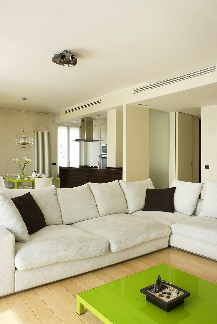 A green coffee table in front of a white corner sofa with brown cushions in an open-plan living-cum-dining area