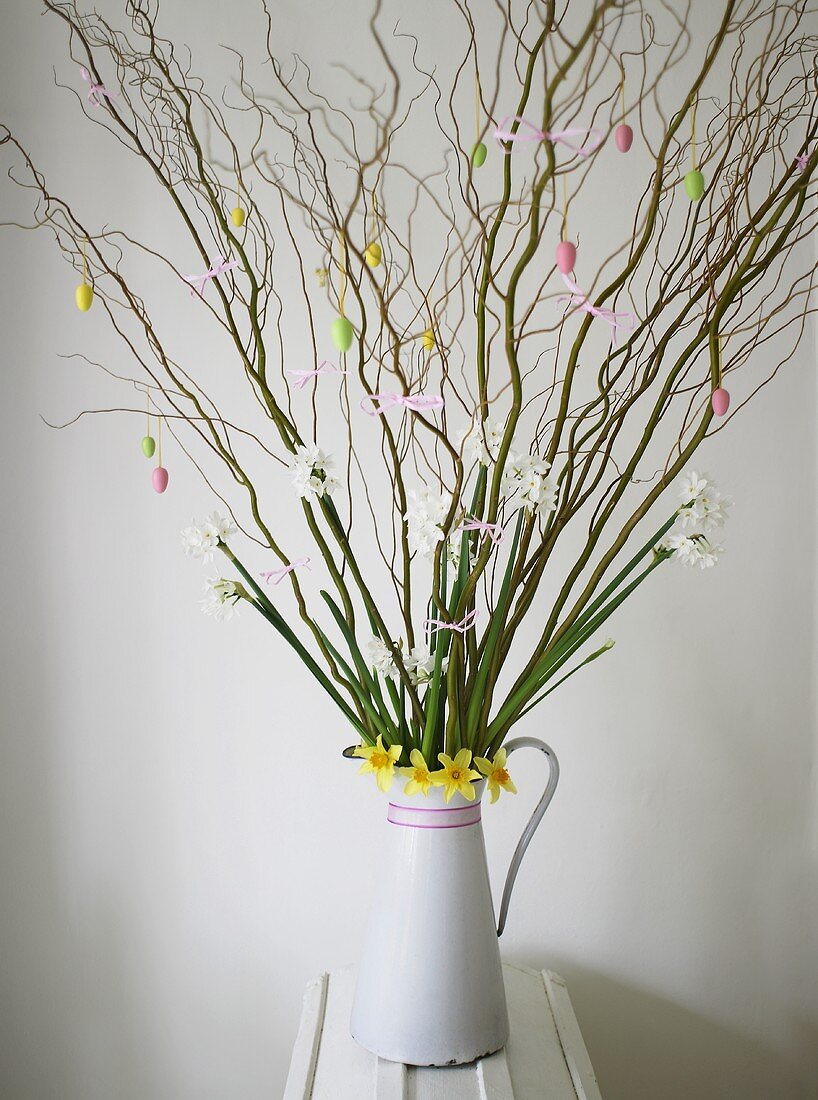 Budding branches and spring flowers with Easter decoration in a white pitcher