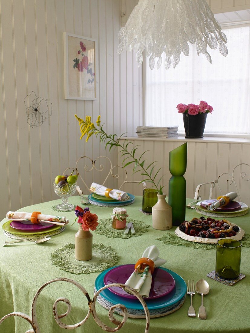Coloured place settings on a green tablecloth in a white, wood panelled dining room