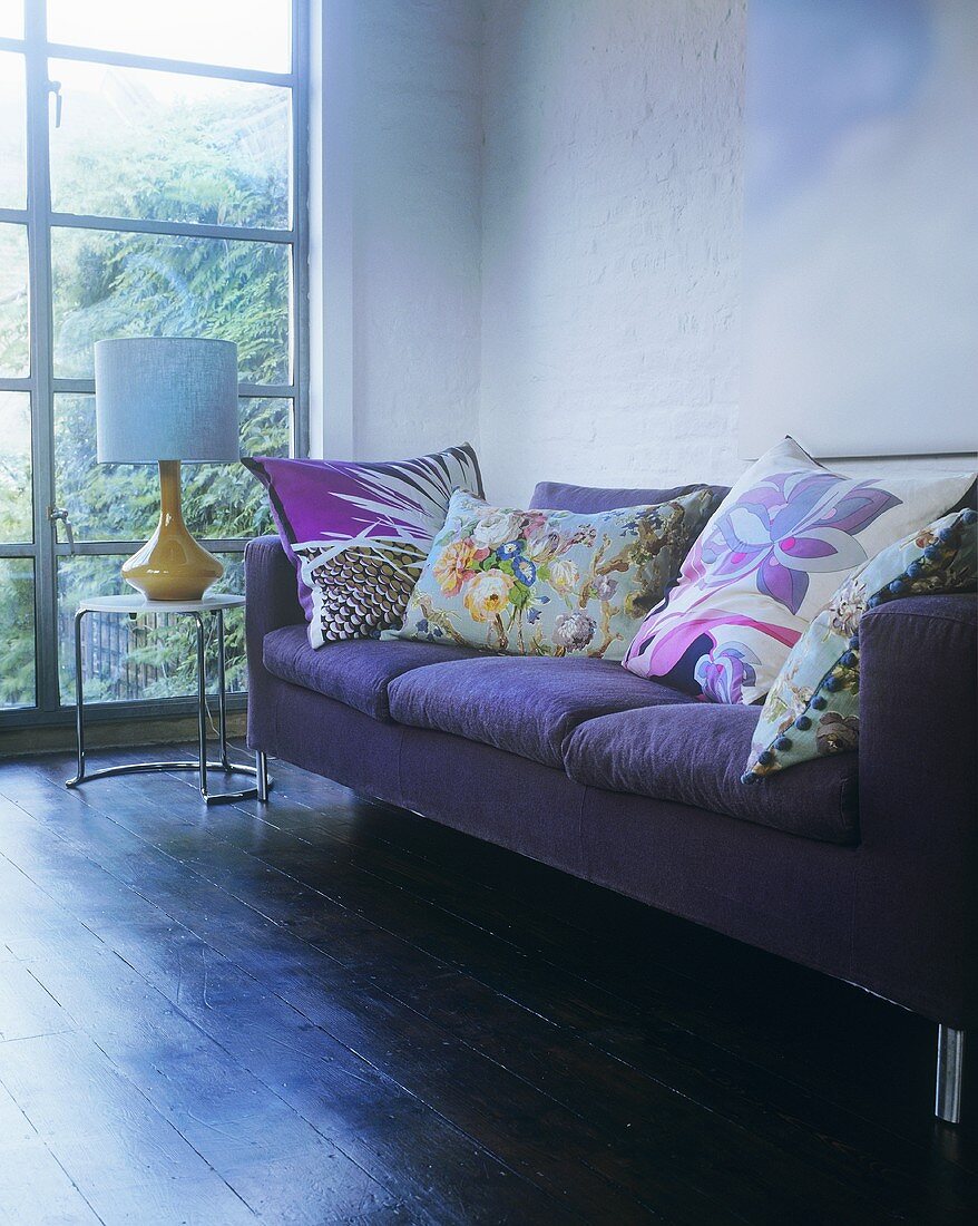 A purple sofa with cushions next to a window