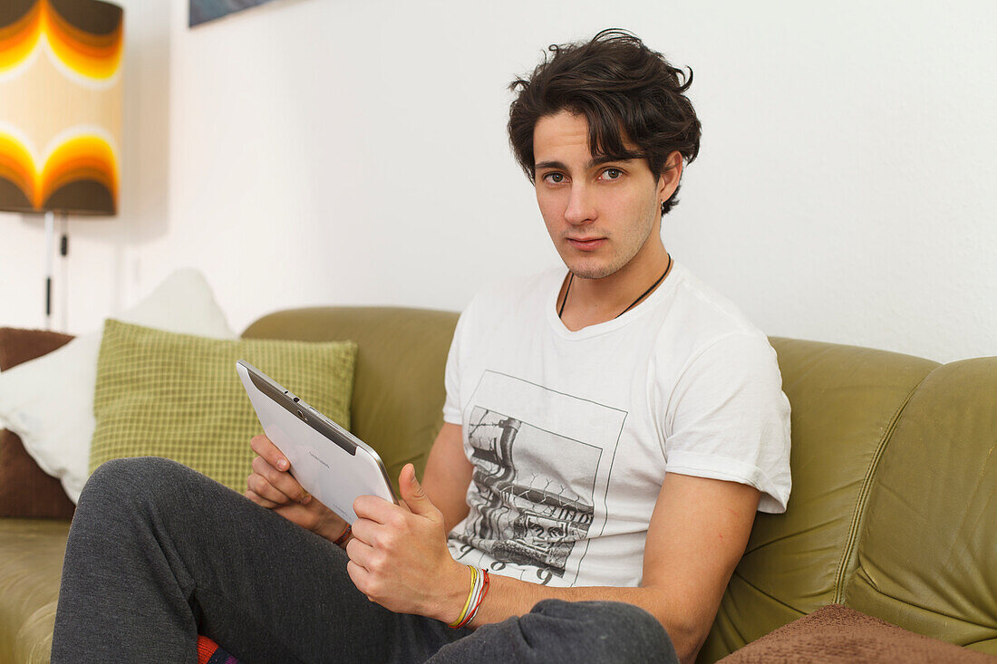 Junger Mann sitzt auf dem Sofa und spielt auf dem Tablet