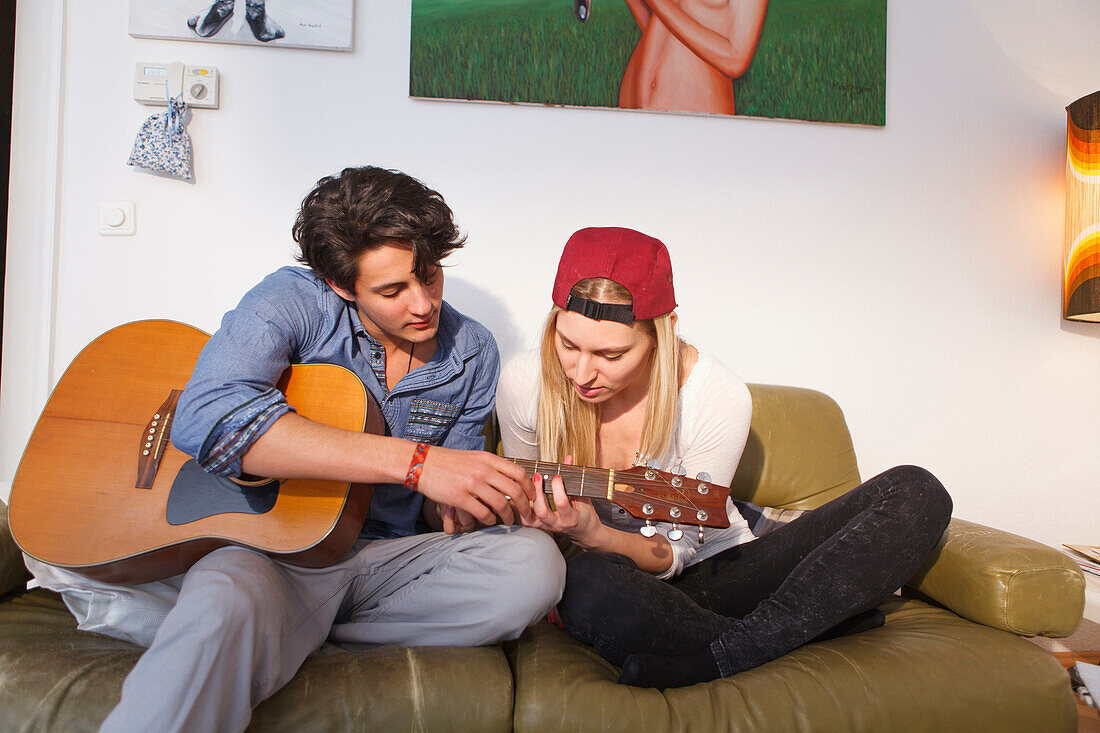 Young couple relaxing on the sofa, playing the guitar