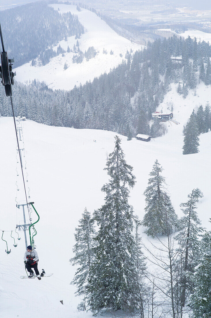 Snowboarder in single chair lift, Kampenwand, Alps, Bavaria, Germany