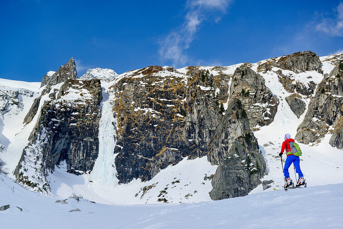 Frau auf Skitour steigt auf Felswand mit Wasserfall zu, Grundschartner, Zillergrund, Zillertaler Alpen, Tirol, Österreich