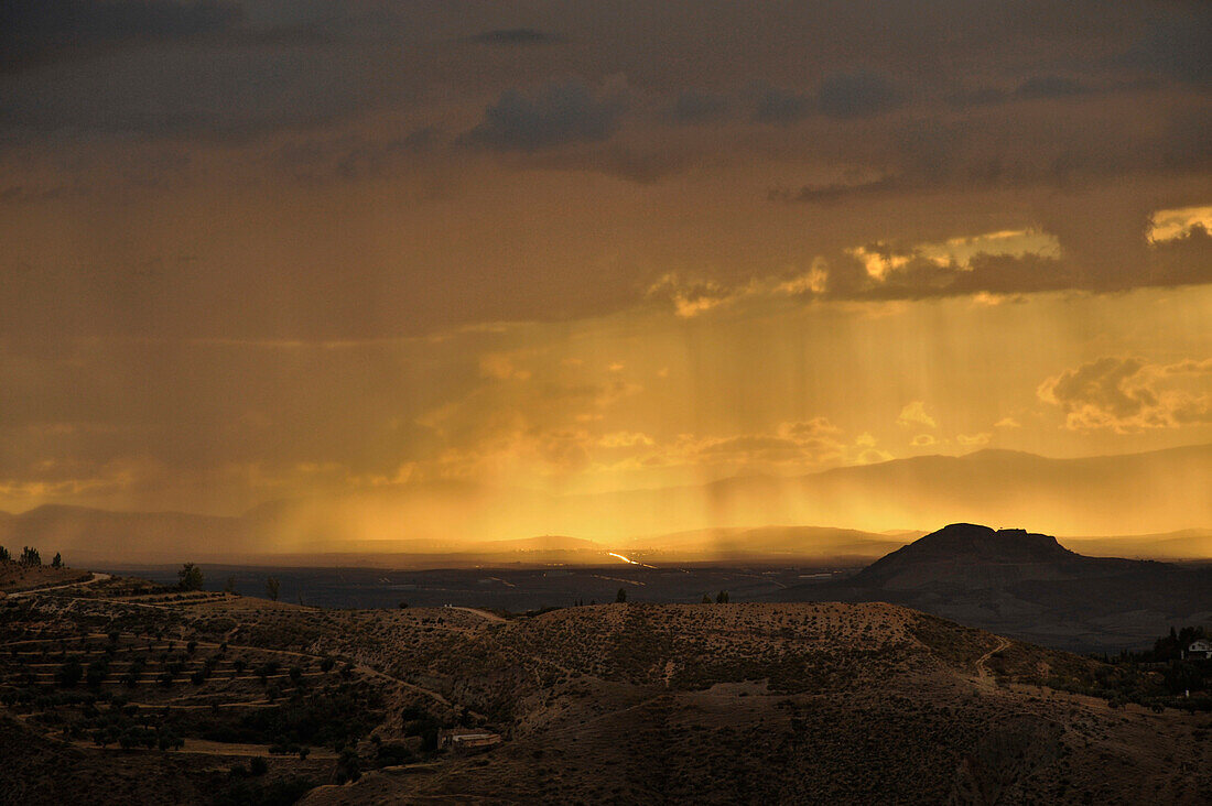 yellow sunrays breaking through clouds, thunderstorm near Granada, seen from Monachil at the foothills of the Sierra Nevada, Andalusia, Spain